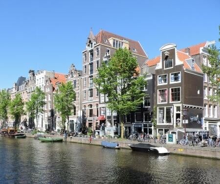Herenhuizen langs de Amsterdamse grachten met boten die aan de kade liggen op een zonnige dag.