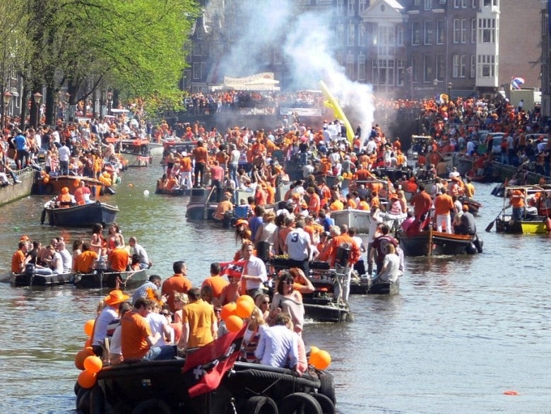 Groepen mensen in het oranje gekleed op verschillende boten tijdens Koningsdag op de Amsterdamse grachten.